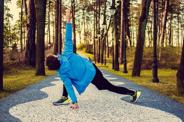 Elastyczny mężczyzna fitness w niebieskiej kurtce sportowej, ćwiczenia na zewnątrz.