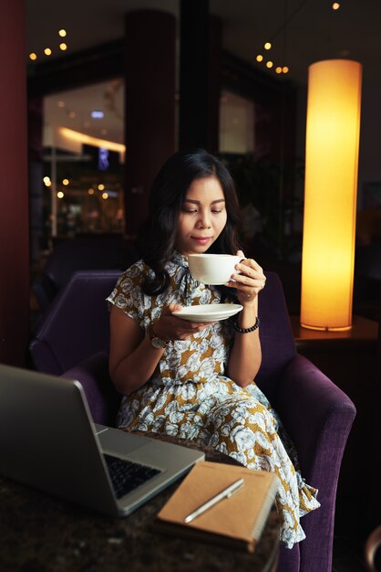 Elegancka Azjatycka kobieta cieszy się cappuccino w kawiarni i laptopu lying on the beach na stole