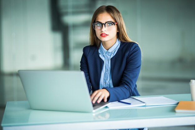 Elegancka i wesoła bizneswoman. Wesoła młoda piękna kobieta w okularach patrząc z uśmiechem siedząc w swoim miejscu pracy