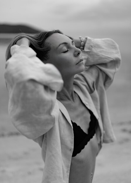 Elegancka kobieta w swobodnym stroju pozuje na samotnej plaży w pochmurną pogodę Czarno-biały