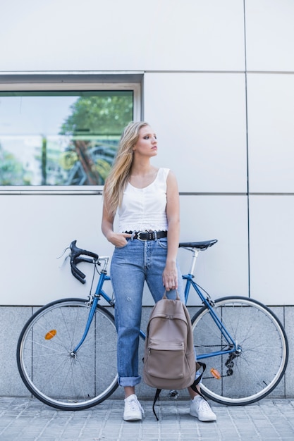 Bezpłatne zdjęcie elegancka młodej kobiety mienia plecaka pozycja przeciw bicyklowi