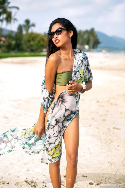 Elegancka modna kobieta pozuje na tropikalnej egzotycznej plaży, luksusowe wakacje, nosi okulary przeciwsłoneczne bikini i stroje plażowe.