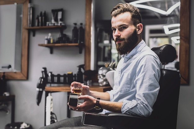 Elegancki mężczyzna z alkoholem pije w zakładzie fryzjerskim