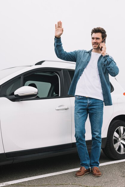 Elegancki młody człowiek stojący w pobliżu nowoczesnego samochodu machając ręką