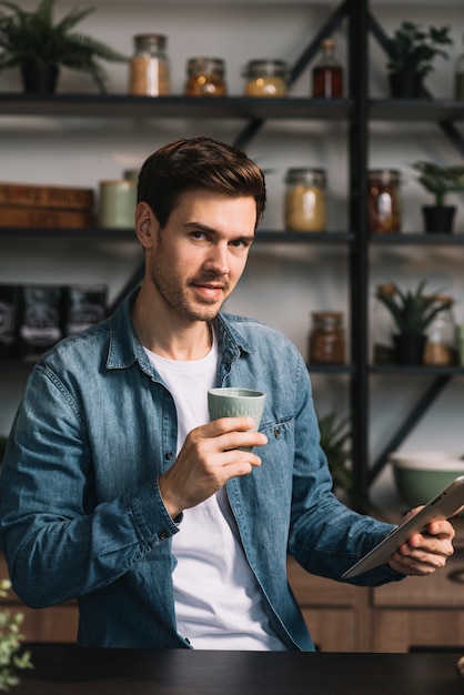 Elegancki młody człowiek trzyma filiżankę kawy i cyfrową pastylkę w rękach