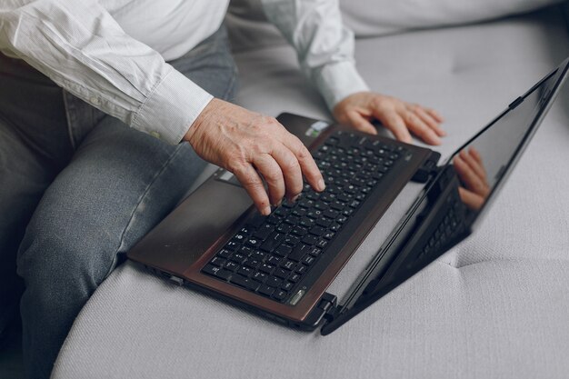 Elegancki stary człowiek siedzi w domu i używa laptopa