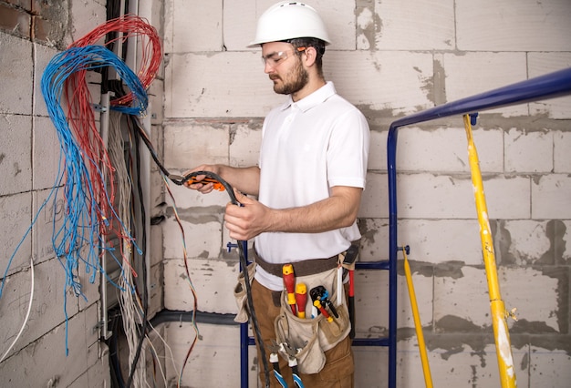 Elektryk pracujący w pobliżu tablicy z przewodami. Instalacja i podłączenie elektryki.