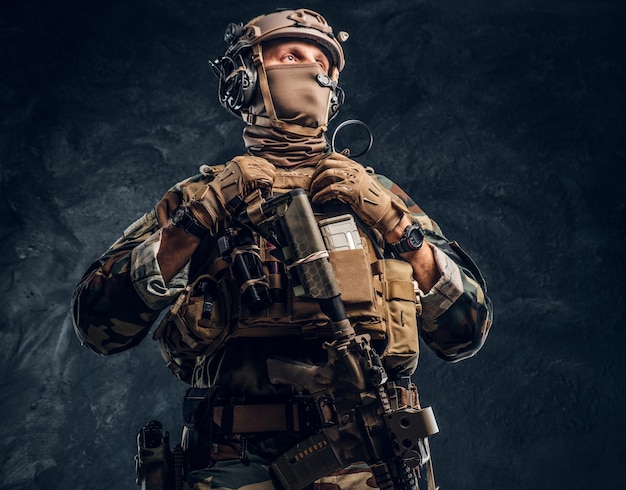 Elitarna jednostka, żołnierz sił specjalnych w mundurze kamuflażowym. Zdjęcie studyjne na tle ciemnej, teksturowanej ściany