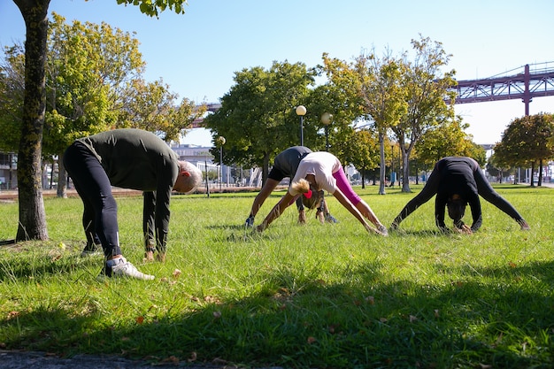 Bezpłatne zdjęcie emeryci, aktywni dojrzali ludzie w strojach sportowych, wykonujący poranne ćwiczenia na trawie w parku, rozciągający mięśnie pleców i nóg. koncepcja emerytury lub aktywnego stylu życia