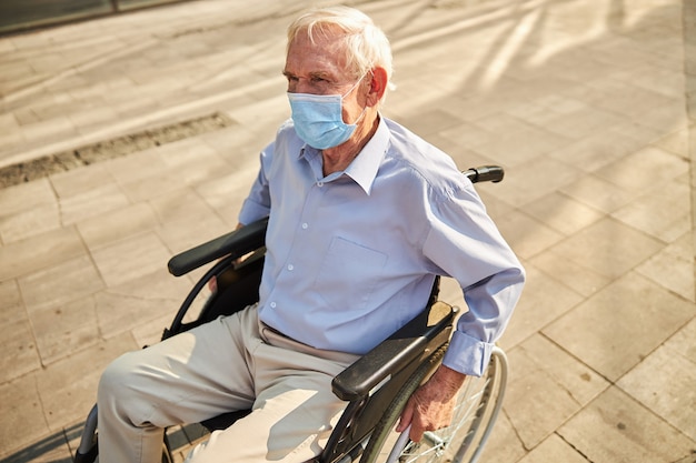 Emeryt w masce z niepełnosprawnością chodzącą na wózku inwalidzkim