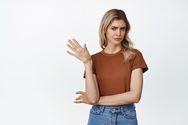 Emocje i gesty Wybredna i sceptyczna blond kobieta mówi „nie machaj ręką” w odmowie gest odrzucając coś z niechęcią stojąc na białym tle