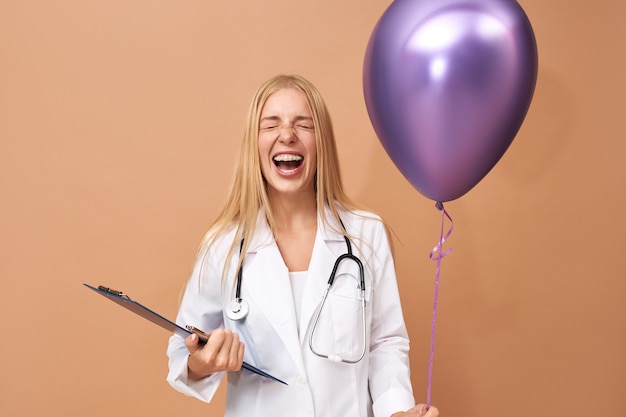 Emocjonalna, Szczęśliwa Młoda Pediatra W Fartuchu Chirurgicznym, Bawiąca Się, śmiejąca Się Z Zamkniętymi Oczami, Gratulująca Jej Małego Chorego Pacjenta Na Urodziny W Szpitalu