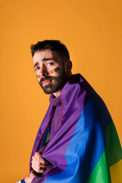 Emocjonalny homoseksualny mężczyzna zawinięty w tęczową flagę LGBT