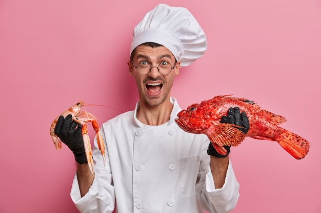 Bezpłatne zdjęcie emocjonalny kucharz pozuje z owocami morza w białym mundurze, głośno krzyczy, zaprasza do swojej restauracji