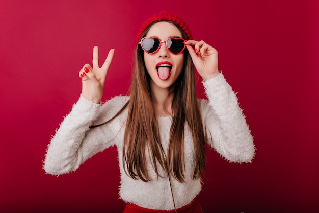 Entuzjastyczna długowłosa dziewczyna nosi fajne okulary przeciwsłoneczne ze znakiem pokoju
