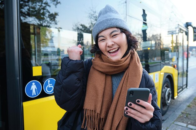 Entuzjastyczna dziewczyna raduje się czyta wiadomość na telefonie komórkowym i świętuje stoiska w pobliżu jej autobusu publicznie