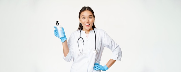 Entuzjastyczna lekarka w mundurze pokazująca profilaktykę mydła do rąk covid19 stojącego na białym tle