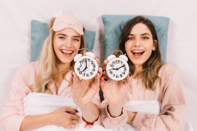Bezpłatne zdjęcie entuzjastyczne kobiety w łóżku pokazujące zegary
