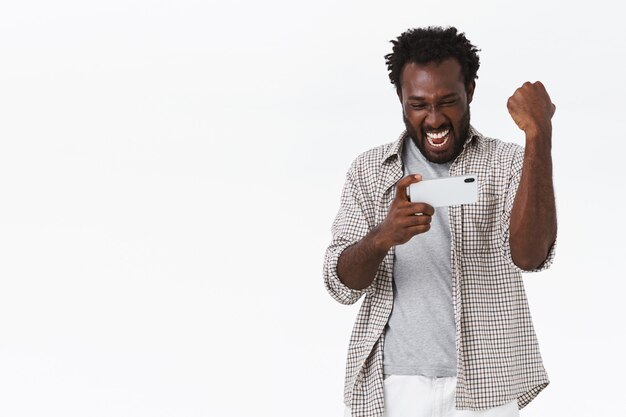 Entuzjastyczny przystojny szczęśliwy Afro-Amerykanin, trzymający smartfon poziomo