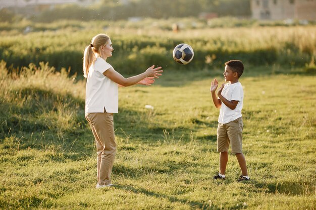 Europejska matka i afrykański syn. Rodzina w letnim parku. Ludzie bawią się piłką.
