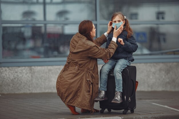 Europejska matka w respiratorze z córką stoi w pobliżu budynku. Rodzic uczy dziecko, jak nosić maskę ochronną, aby uchronić się przed wirusem