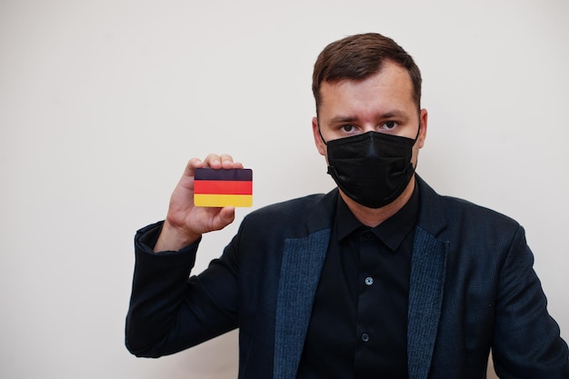 Bezpłatne zdjęcie europejski mężczyzna nosi czarną maskę formalną i chroni twarz trzymaj kartę flagi niemiec na białym tle europa koronawirus covid koncepcja kraju