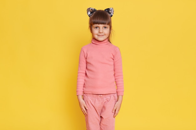 Bezpłatne zdjęcie europejskie urocze małe dziecko płci żeńskiej pozuje z uszami kota na żółtym tle