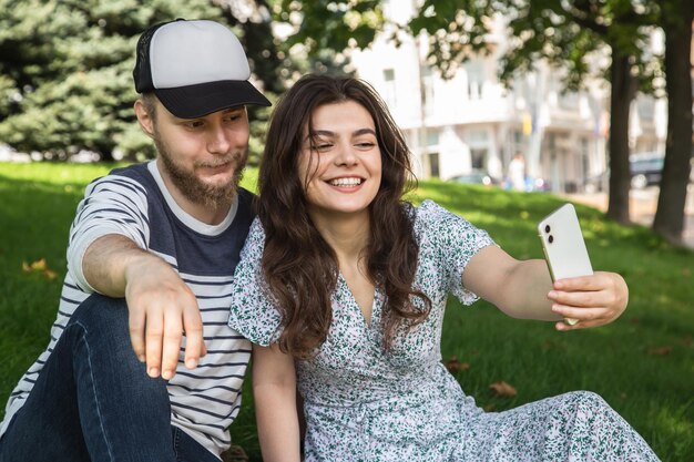 Facet i dziewczyna robią sobie selfie siedząc na trawie w parku