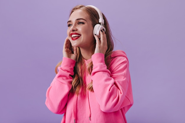 Fajna dziewczyna w różowej bluzie z kapturem słuchająca muzyki w białych słuchawkach