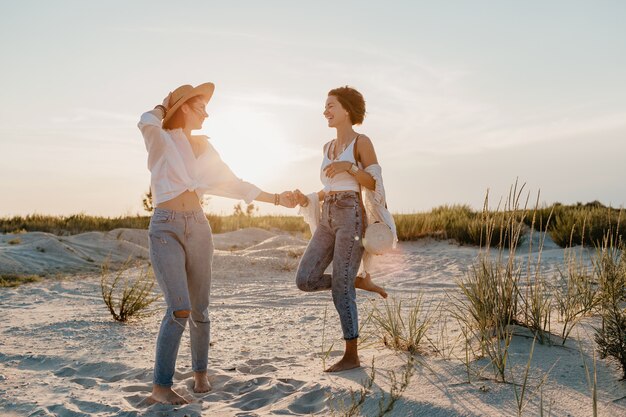 Fajne dwie młode kobiety bawiące się na plaży o zachodzie słońca, gejowskie lesbijki kochają romans