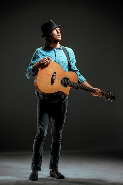 Bezpłatne zdjęcie fajny facet stojący z gitarą na ciemnej ścianie