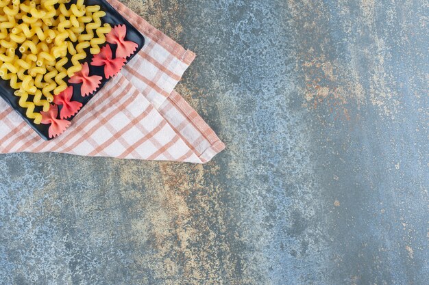 Farfalle i kędzierzawy makaron na talerzu, na ręczniku, na marmurowym tle.
