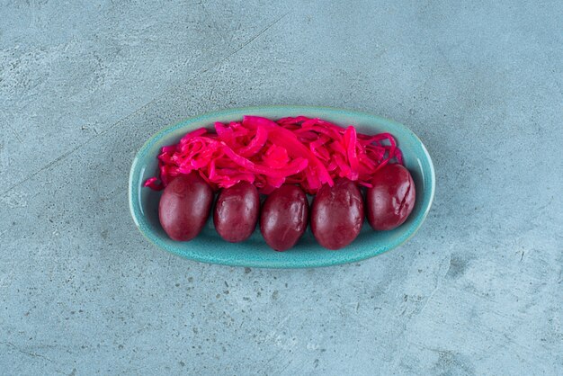 Fermentowana czerwona kapusta kiszona ze śliwkami na talerzu, na niebieskim stole.