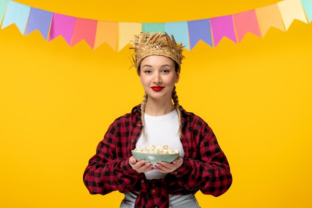 Festa junina blond śliczna dziewczyna w słomkowym kapeluszu brazylijski festiwal z kolorowymi flagami trzymającymi popcorn