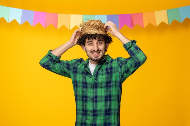 Festa junina młody uroczy facet w słomkowym kapeluszu i kolorowe flagi brazylijski festiwal trzymający kapelusz