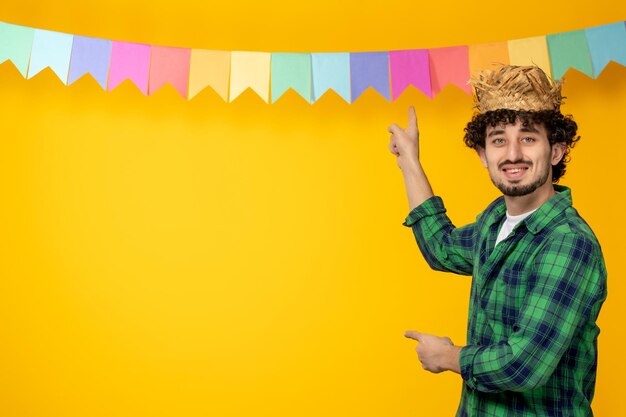 Festa junina młody uroczy facet w słomkowym kapeluszu i kolorowe flagi brazylijski festiwal wskazujący na flagi