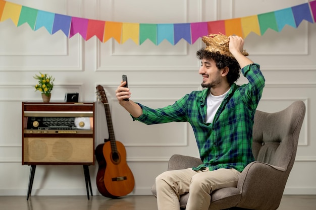 Bezpłatne zdjęcie festa junina słodki młody facet w słomkowym kapeluszu z retro radiem i kolorowymi flagami robi selfie