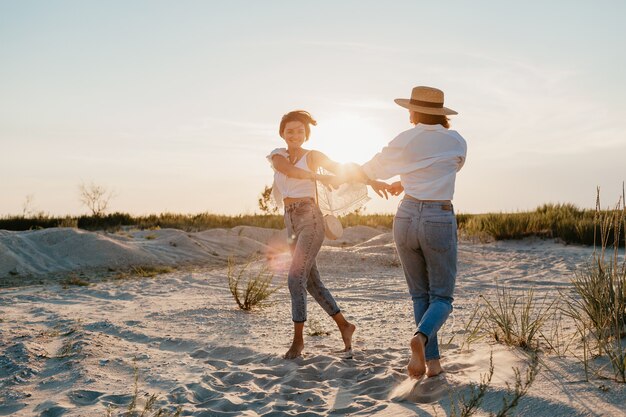 Figlarne dwie młode kobiety bawiące się na plaży o zachodzie słońca, homoseksualne lesbijki kochają romans