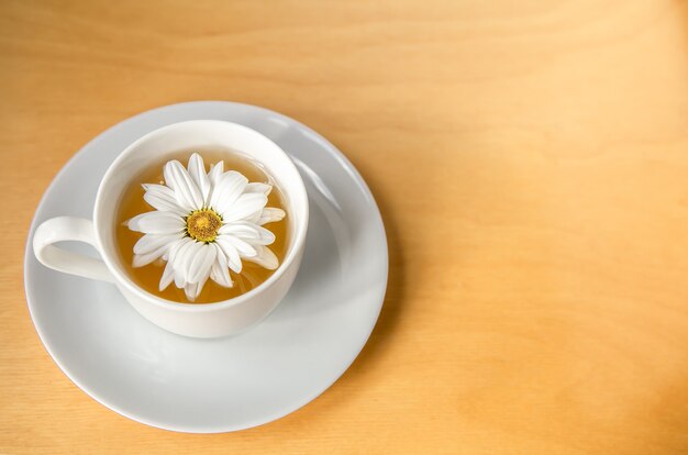 Filiżanka herbaty z kwiatem rumianku na drewnianej przestrzeni kopii tła