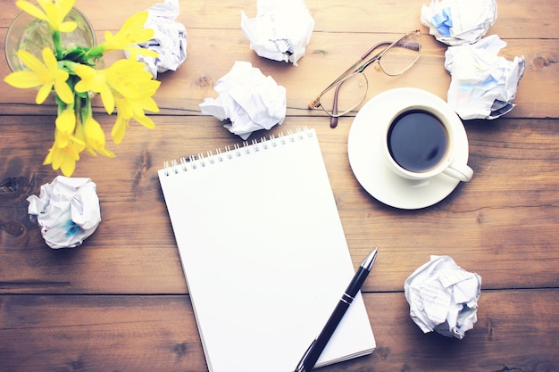 Filiżanka kawy, długopis, notatnik, papiery, okulary i kwiat na drewnianym stole