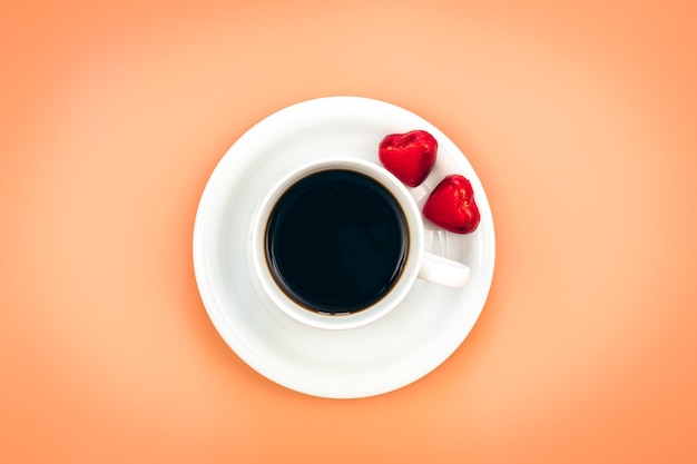 Bezpłatne zdjęcie filiżanka kawy i cukierki w kształcie serca na pomarańczowym tle leżały płasko