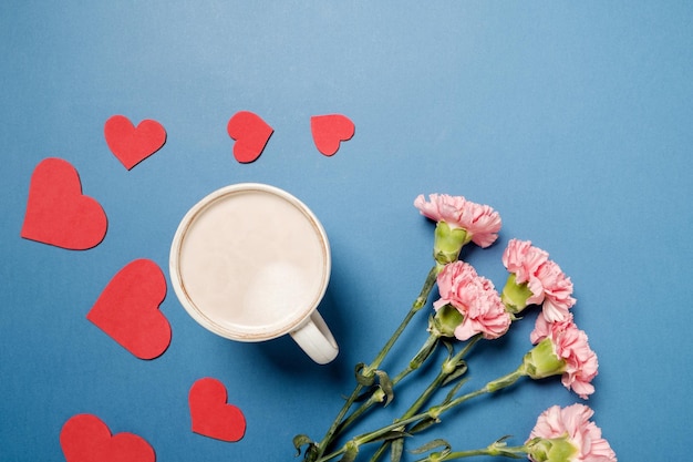 Bezpłatne zdjęcie filiżanka kawy i różowy goździk z czerwonym sercem na niebieskim stole widok z góry
