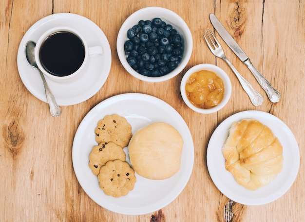 Filiżanka kawy; jagody; dżem; chleb; bułka i ciasteczka na stole