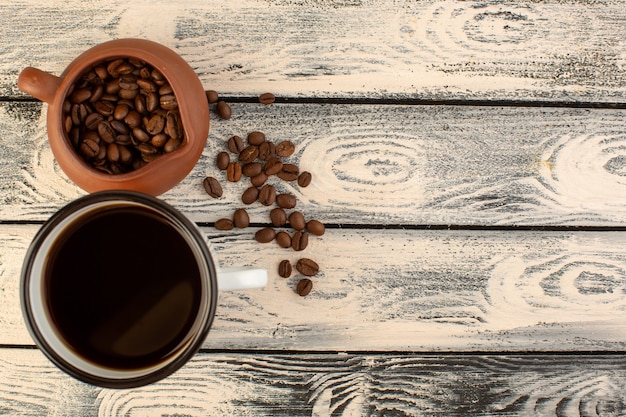 Filiżanka kawy z brązowymi ziarnami kawy z widokiem z góry na szarym rustykalnym biurku pije kawę w kolorze