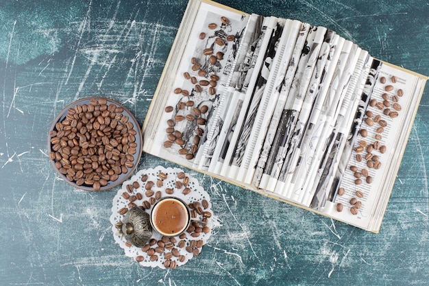 Bezpłatne zdjęcie filiżanka spienionej kawy, talerz ziaren kawy i książka na marmurowym stole.