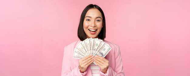 Finansowy mikrokredyt i koncepcja ludzi Szczęśliwa uśmiechnięta azjatycka bizneswoman pokazująca pieniądze w dolarach stojących w garniturze na różowym tle