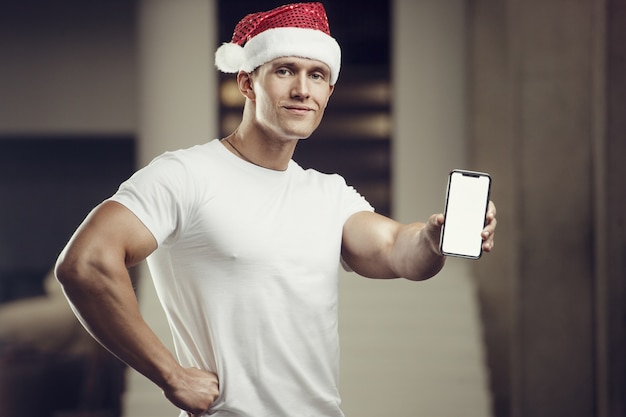 Fitness mężczyzna w stroju czapki świętego mikołaja w siłowni z telefonem komórkowym. wesołych świąt i nowego roku koncepcja