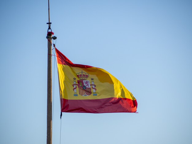 Flaga narodowa Hiszpanii macha na masztem nad jasne błękitne niebo