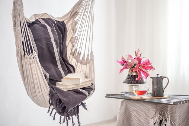 Fotel hamakowy w stylu boho z książkami i czajnikiem oraz filiżanką herbaty. Pojęcie wypoczynku i domowego komfortu.