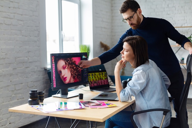 Fotograf i grafik pracujący w biurze z laptopem, monitorem, tabletem graficznym i paletą kolorów.